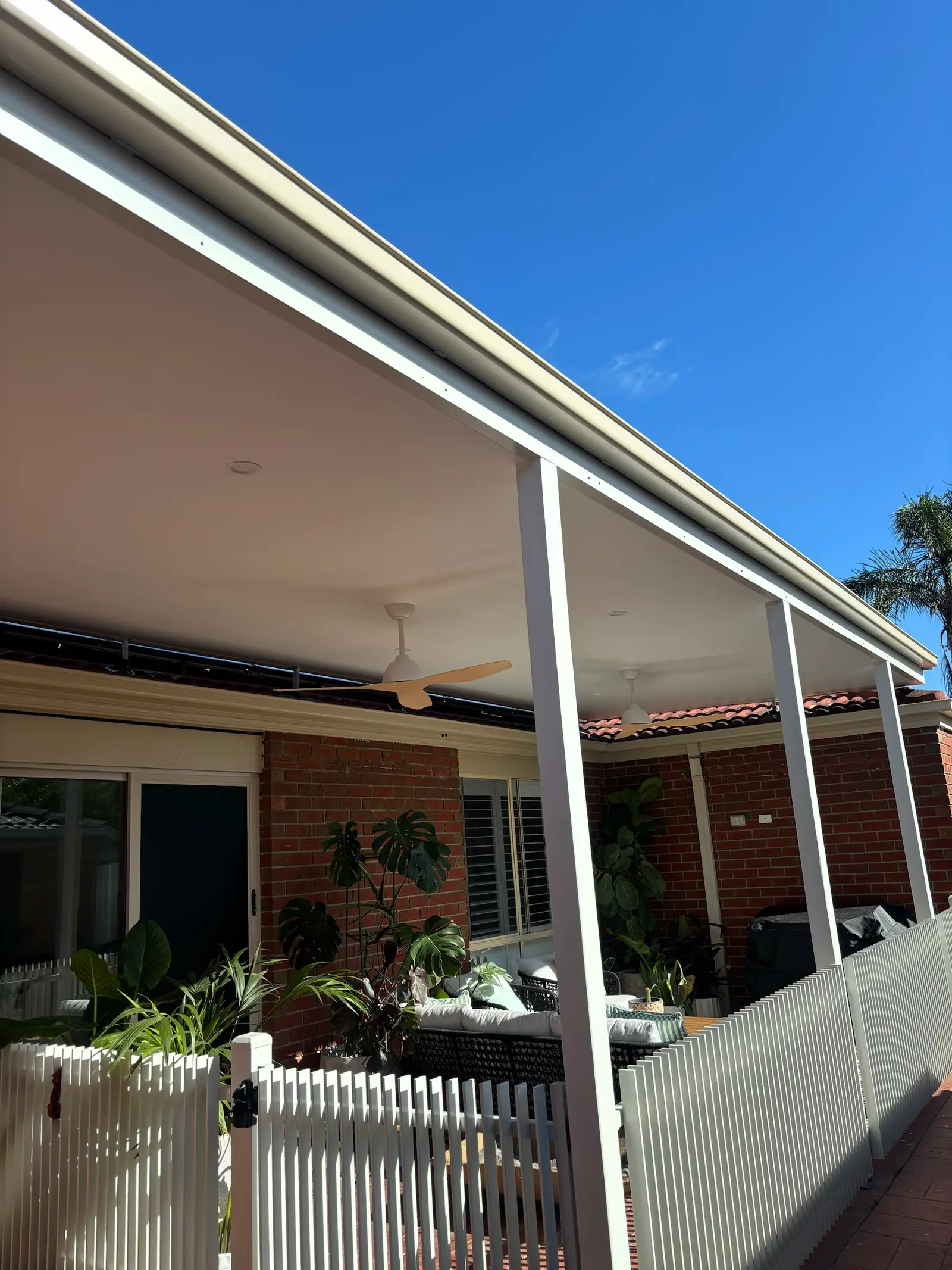 Looking up at the verandah's lined ceiling, fascia and square posts against a blue sky