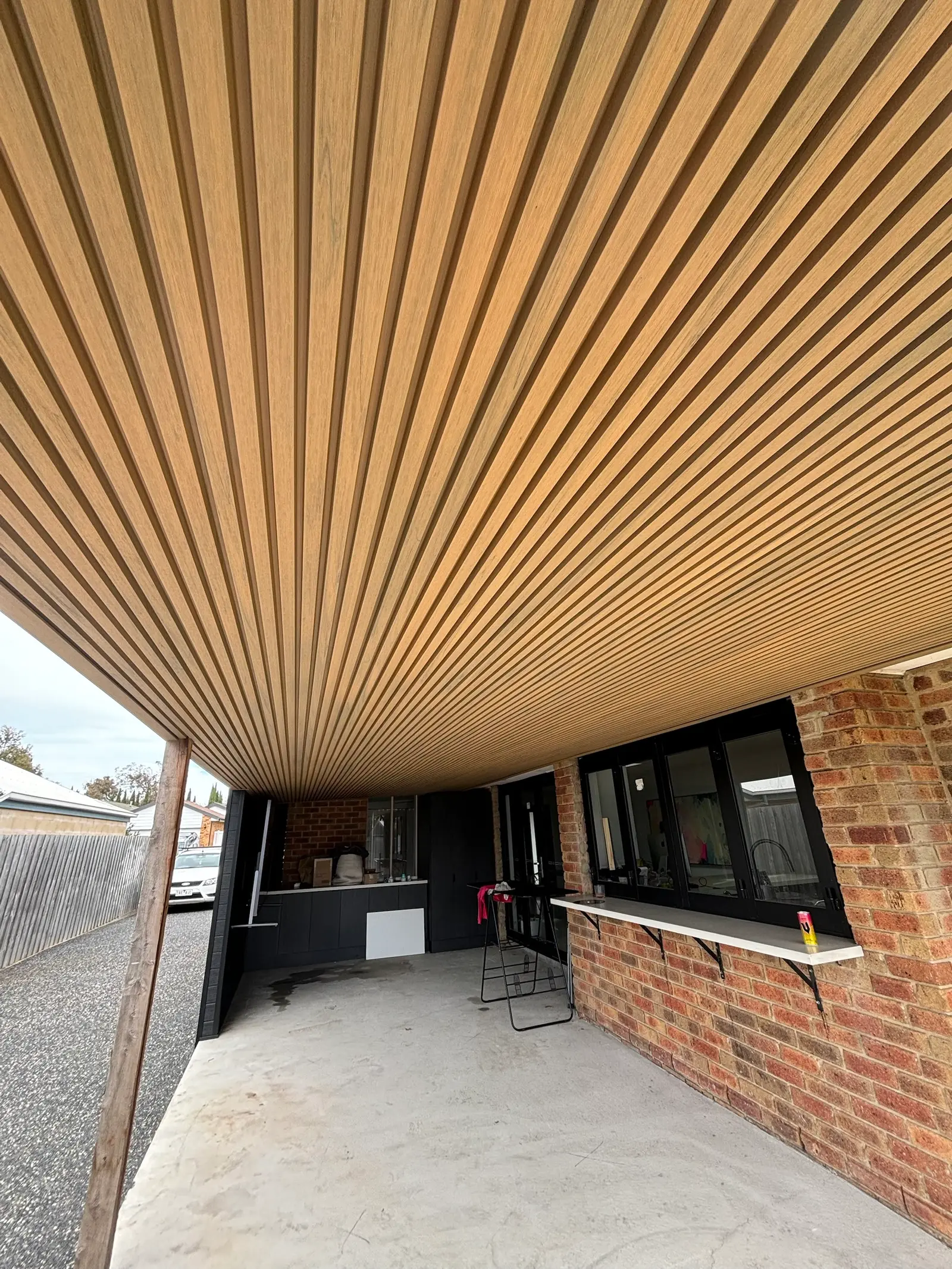 Timber-look slat ceiling over a carport with an outdoor kitchen, servery window and brick piers