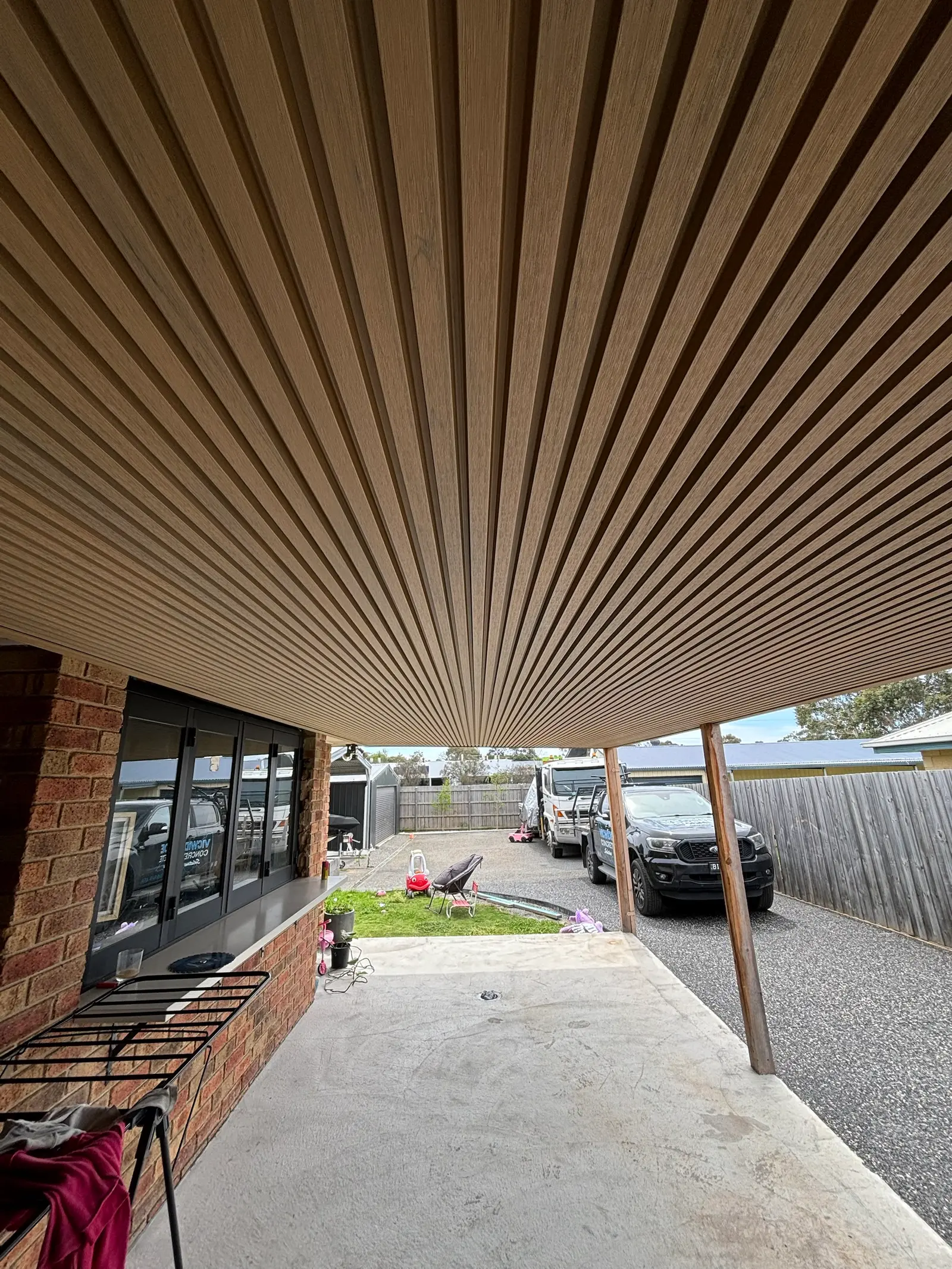 Looking along the slat-lined carport ceiling towards the driveway, with a timber post and bifold servery window