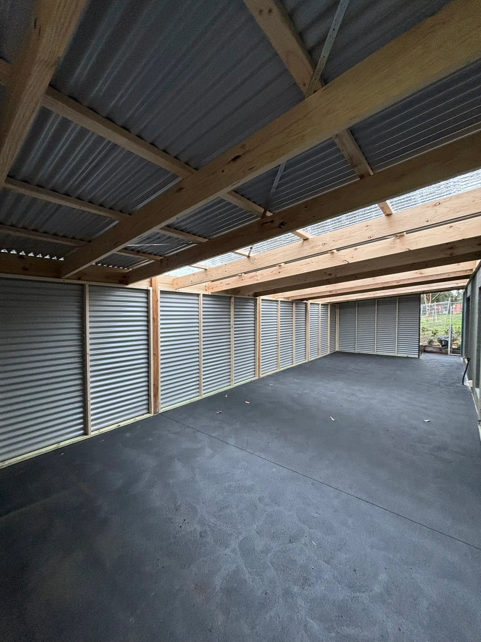 Inside the clad structure: timber wall framing, exposed rafters and translucent roof sheets above a long concrete slab